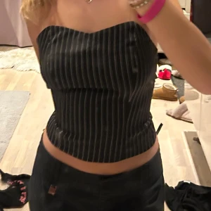 Svart tubtopp med vita ränder - Snygg svart tubtopp med smala vita ränder. Perfekt för en stilren look. Toppen är axelbandslös och har en tight passform som framhäver figuren.