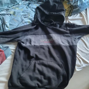 Svart hoodie från McKenzie - Säljer en svart hoodie från McKenzie med en stor ficka framtill och logotypen broderad över bröstet. Den har en bekväm passform och är perfekt för kyligare dagar. Huvan ger extra värme och stil. Perfekt för en avslappnad look!