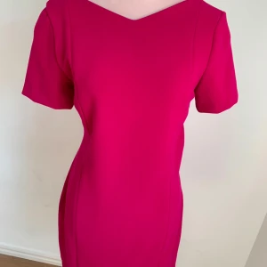 Rosa klänning med svart spetsdetalj - Snygg rosa klänning med korta ärmar och en v-ringad rygg. Den har en vacker svart spetsdetalj på ryggen som ger en elegant touch. Perfekt för en kväll ute eller en speciell tillställning.