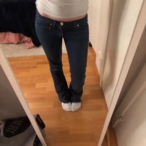 Mörkblå jeans från 7 For All Mankind - Snygga mörkblå jeans från 7 For All Mankind med låg midja och bootcut-stil. De har klassiska fem fickor och en knappgylf med dragkedja. Perfekta för en avslappnad look. Passar mig som är 165cm.