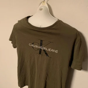 Olivgrön t-shirt från Calvin Klein Jeans - Snygg olivgrön t-shirt från Calvin Klein Jeans med det ikoniska CK-logotypen tryckt på framsidan. Perfekt för en avslappnad stil. T-shirten har en klassisk rund hals och korta ärmar. Storlek 164.