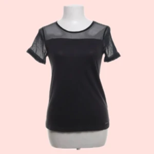 Svart topp med meshdetaljer - Snygg svart topp med korta ärmar och har genomskinligt tyg på axlar och ärmar. Perfekt för en stilren look med en twist. Toppen har en rund halsringning och en normal passform. Står xs men passar mig som är s.