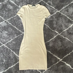 Beige ribbad klänning från New Yorker , tight och stretchig  - Säljer en stilren beige ribbad klänning från New Yorker i storlek XXS. Klänningen har en tight passform och korta ärmar, perfekt för en minimalistisk look. Den är gjord i ett mjukt och stretchigt material som sitter bekvämt på kroppen. Perfekt för att klä upp eller ner beroende på tillfälle.