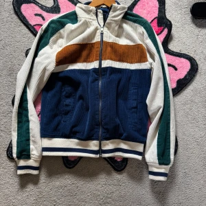 Flerfärgad jacka med dragkedja - Säljer en cool jacka med dragkedja i flera färger: marinblå, vit, brun och grön. Jackan har ribbade muddar och en sportig look med långärmade ärmar. Perfekt för en avslappnad stil.