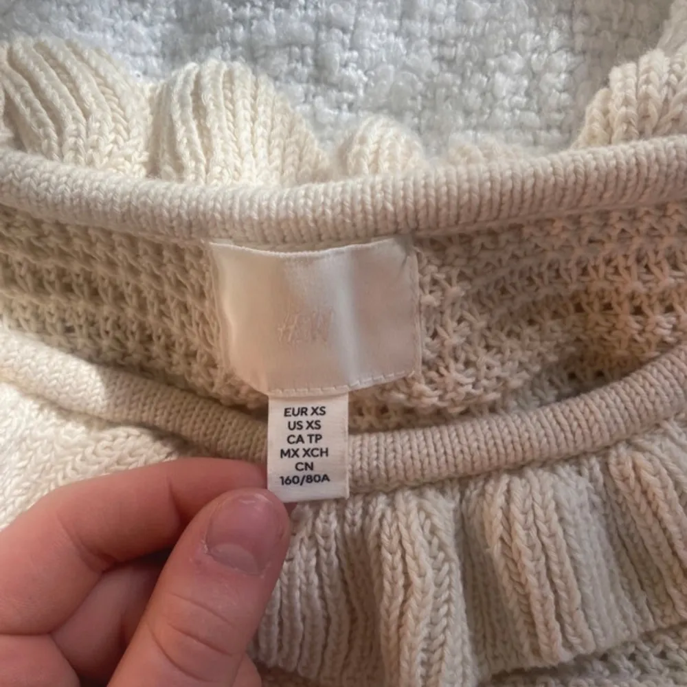Charmig beige stickad topp från H&M med volangdetaljer runt halsringningen. Tveka inte att höra av dig👏🏼😄. Puserot.