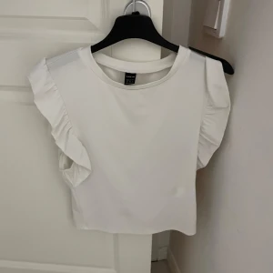 Vit blus med volangärmar  - Säljer en stilren vit blus  med volangdetaljer på ärmarna. Perfekt för en chic och elegant look. Blusen har en rund halsringning och är tillverkad i ett mjukt material.