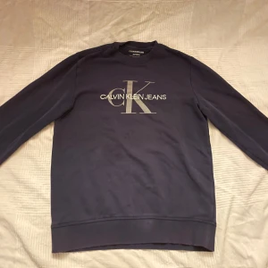 Calvin Klein tröja  - Snygg och stilren Calvin Klein-tröja i hög kvalitet. Klassisk design med diskret logotyp, perfekt för både vardag och avslappnade tillfällen. Skön passform och mjukt material som ger en bekväm känsla.