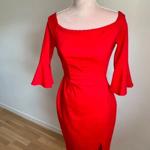Röd klänning med volangärmar - Snygg röd klänning med volangdetaljer på de trekvarts långa ärmarna. Klänningen har en figurnära passform och en liten slits framtill. Perfekt för en elegant look.