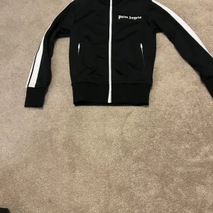 Svart träningsjacka från Palm Angels - Klassisk Palm angels kofta i storlek XXS men passar XS. Tröjan är knappt använd och i nyskick. Nypris:4000kr. Bara att höra av sig vid minsta fundering.