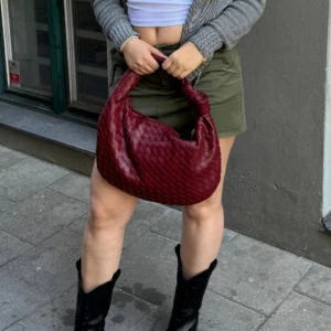 Röd flätad axelväska - Snygg röd axelväska i flätat mönster. Perfekt för att ge din outfit en färgklick. Väskan har en mjuk och rundad form med ett bekvämt handtag. Som ny!