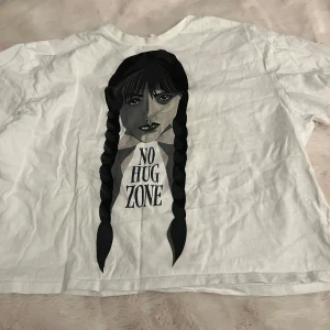 Vit t-shirt med Wednesday på  - Säljer en vit t-shirt med ett tryck av Wednesday och texten 'No Hug Zone'. T-shirten har en avslappnad passform och korta ärmar. Perfekt för en cool och avslappnad stil.