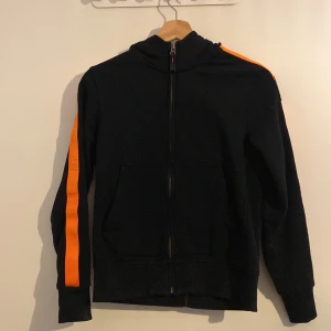 Svart fleecejacka från Parajumpers - Säljer en svart fleecejacka från Parajumpers med orangea ränder längs ärmarna. Jackan har en dragkedja framtill och en broderad logga på ärmen. Perfekt för kyliga dagar! Tröjan är o storlek XS och byxorna i storlek S. Orginal priset för de båda ligger på 4899. Jag vill ha 3500 för båda två 💗