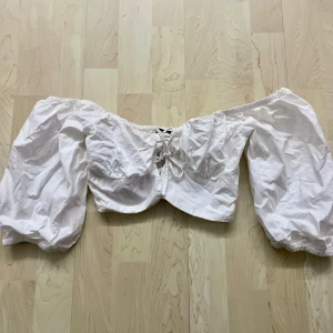 Vit offshoulder blus - Charmig vit offshoulder blus med puffiga trekvartsärmar och snörning framtill. Perfekt för en somrig look med elastisk rygg för bekväm passform.