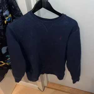 Mörkblå tröja från Polo Ralph Lauren - Säljer en stilren mörkblå tröja från Polo Ralph Lauren med det klassiska röda broderade logotypen på bröstet. Tröjan har långa ärmar och en rund halsringning. Perfekt för en avslappnad och snygg look.