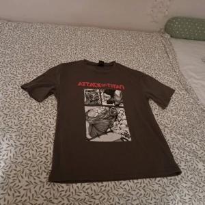 Grön/brun Attack on Titan t-shirt från Romwe - Säljer en brun/grön oversized t-shirt från Romwe med ett coolt Attack on Titan-tryck i svart och vitt. T-shirten har korta ärmar och är perfekt för fans av serien. Storlek S/A 36. Passar perfekt för en avslappnad stil.