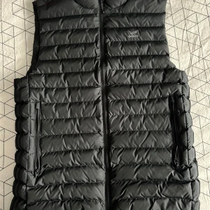 Svart dunväst från Adidas - Säljer en stilren svart dunväst från Adidas. Västen har en dragkedja framtill och två praktiska fickor med dragkedjor. Perfekt för lager-på-lager under kyligare dagar. Adidas-loggan är diskret placerad på bröstet. Använd 2-3 gånger. Köpt för 1200 fast säljer västen för 400kr