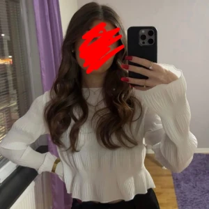 Vit ribbad blus - Säljer en stilren vit blus med ribbad struktur och långa ärmar. Blusen har en lätt volangdetalj vid nederkanten som ger en feminin touch. Perfekt för att klä upp eller ner beroende på tillfälle.