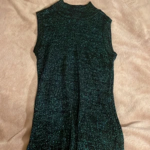 Glittrig ärmlös bluse - Snygg glittrig top i mörkgrön nyans. Den är ärmlös med en ribbad struktur som ger en cool look. Perfekt för att sticka ut på festen! ✨
