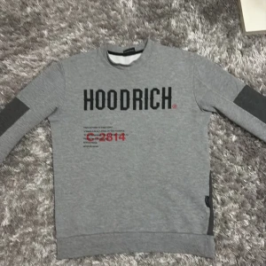 Grå sweatshirt från Hoodrich - Säljer en grå sweatshirt från Hoodrich med tryck både fram och bak. Tröjan har långa ärmar och en dragkedja vid nederkanten. Perfekt för en avslappnad stil. Köpte den för 800 kr pris kan diskuteras 