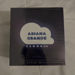 Ariana Grande Cloud 2.0 Intense Parfym - Upptäck Ariana Grande Cloud 2.0 Intense, en eau de parfum med en volym på 100 ml. Förpackningen har en stilren design med en molnformad logotyp och en bild av artisten. Perfekt för den som älskar en intensiv och unik doftupplevelse. Oanvänd fortfarande i plast.