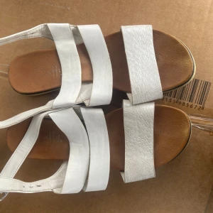 Vita sandaler med klack - Snygga vita sandaler med breda remmar och klack. Sandalerna har en texturerad yta på vissa remmar och en justerbar rem runt ankeln. Perfekta för sommarens varma dagar.