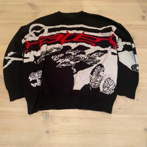 Stickad tröja - Säljer en svart stickad tröja med ett unikt grafiskt mönster i rött och vitt. Tröjan har långa ärmar och en avslappnad passform. Skönt material. Skriv för frågor och mått osv