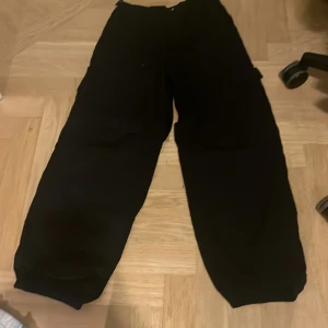 Svarta byxor med resårmidja - Svarta byxor med resårmidja och justerbara spännen. Perfekta för en avslappnad stil. Byxorna har en loose passform och är tillverkade i ett bekvämt material.