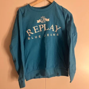 Blå sweatshirt från Replay - Säljer en snygg blå sweatshirt från Replay med tryck 'Replay Blue Jeans' på framsidan. Tröjan har långa ärmar och en rund halsringning. Perfekt för en avslappnad stil.