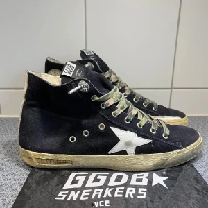  Golden Goose High Top - Snygga svarta sneakers från Golden Goose med vit stjärndetalj på sidan. Skorna har en unik design med kamouflagemönstrade snören och dragkedja på sidan för enkel påtagning. Sulan har en vintage-look som ger en cool stil. Skriv för frågor. Pris kan diskuteras 