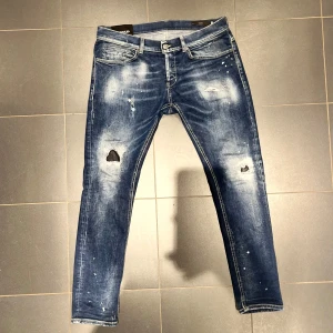 Dondup George - Snygga blå jeans från Dondup med slitna detaljer och en cool tvättad look. De har en klassisk femficksdesign och knappgylf. Perfekta för en avslappnad stil med en touch av edge. Hör av er vid frågor eller funderingar! Mvh
