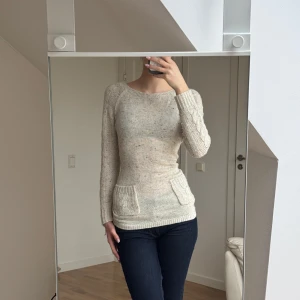 Beige stickad tröja med fickor - Säljer en mysig beige stickad tröja med kabelstickade detaljer och praktiska fickor framtill. Tröjan har långa ärmar och en rund halsringning, perfekt för kyligare dagar. Passar bra till jeans eller kjol för en avslappnad look.