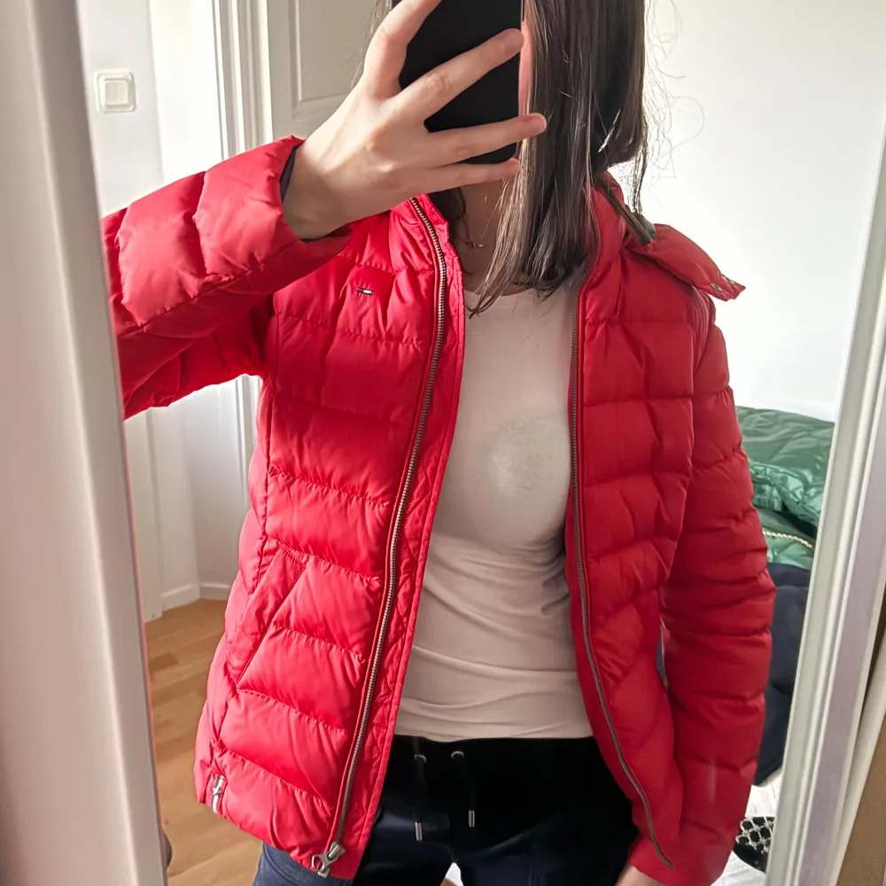 Säljer en snygg röd dunjacka från Tommy Hilfiger. Jackan har en dragkedja framtill och långa ärmar. Den har en liten logotyp på bröstet och en hög krage för extra skydd mot vind samtidigt som den är väldigt skön!. Takit.