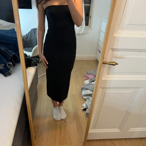 Svart axelbandslös klänning - Snygg svart axelbandslös klänning i en tight passform. Perfekt för en elegant look. Klänningen är enkel och stilren, vilket gör den lätt att matcha med olika accessoarer.
