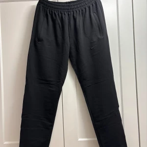 Nike svarta mjukis  - Snygga svarta mjukisbyxor med elastisk midja och praktiska sidofickor. Perfekta för en avslappnad stil. Byxorna har en enkel design med en bakficka och är gjorda i ett mjukt material för extra komfort.