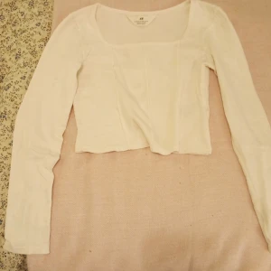 Vit ribbad topp från H&M - Säljer en stilren vit ribbad topp från H&M. Toppen har en tight passform med långa ärmar och en fyrkantig halsringning. Perfekt för lager-på-lager eller som den är. Hör av dig vid intresse!