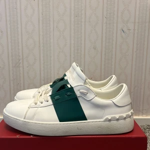 Valentino Garavani sneakers i vitt och grönt - Snygga Valentino Garavani sneakers i vitt med gröna detaljer. Skorna har en stilren design med snörning och en bred grön rem över ovansidan. Perfekta för en trendig look. Använda en gång och är i mycket bra skick, Valentino Box är med och pris kan diskuteras!