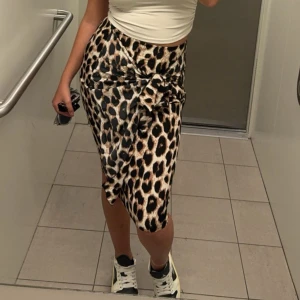 Leopardmönstrad kjol med knyt - Snygg leopardmönstrad kjol med knyt i midjan. Kjolen har en omlott-design som ger en stilren look. Perfekt för att sticka ut med ett djärvt mönster.