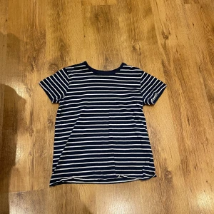 Randig t-shirt i ekologisk bomull - Säljer en randig t-shirt från Basic i ekologisk bomull. T-shirten är blå med vita ränder och har en klassisk rund hals. Perfekt för en avslappnad stil.