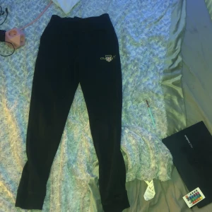 Svarta mjukisbyxor från GANT - Säljer ett par svarta mjukisbyxor från GANT. Byxorna har en bekväm passform med resår i midjan och en liten logga på sidan. Perfekta för en avslappnad stil.