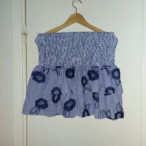 Blå och vit randig kjol från Holly & Whyte - Säljer en söt blå och vit randig kjol från Holly & Whyte by Lindex. Kjolen har ett elastiskt midjeband och är dekorerad med broderade blommor i mörkblått. Perfekt för en somrig look! 🌸