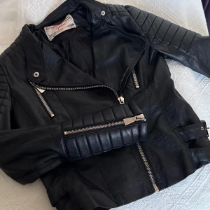 Svart skinnjacka - Snygg svart skinnjacka med coola detaljer som dragkedjor och quiltade axlar och armar. Knappt använd, i nytt skick