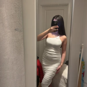 Vit one shoulder klänning - Snygg vit enaxlad klänning med en figurnära passform och stretchigt material. Klänningen har en elegant design med smala axelband och en smickrande scrunch både på sidorna av höfterna och bak.