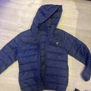 Blå pufferjacka med huva - Säljer en blå pufferjacka från Lyle & Scott med huva och dragkedja. Jackan har ett quiltat mönster och är perfekt för kyligare dagar. Den har långa ärmar och en liten logotyp på bröstet. I afärr kostar jackan 1199kr men jag säljer den för 479kr. Har även mer varor såsom Burberry halsdukar och skor i lageret.