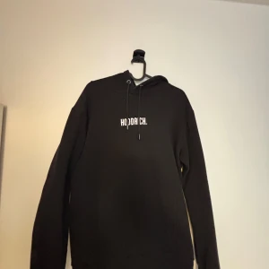 Svart hoodie från Hoodrich - Säljer en svart hoodie från Hoodrich i storlek medium. Den har en klassisk design och en enkel logga på bröstet. Perfekt för en avslappnad stil.