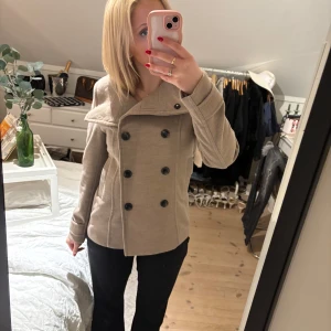 Kort beige kappa med dubbelknäppning  - Kort beige kappa som är perfekt till våren. Använd cirka 2 ggr. Går även att knäppa den hela vägen upp, så att kragen ”står upp” 🥰