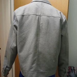 Grå jacka med dragkedja - Säljer en stilren grå jacka med dragkedja och två stora fickor framtill. Jackan har en klassisk krage och långa ärmar, perfekt för kyligare dagar. Enkel och snygg design som passar till det mesta. Köpt för 1200kr säljs pga av att min son inte använder den.