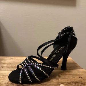 Svarta dansskor med strassdetaljer - Eleganta svarta dansskor från Manuel Reina med glittrande strassdetaljer. Skorna har en smal remdesign och en bekväm klack. Nypris 2100:-