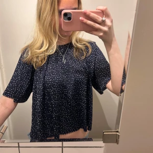 Mörkblå prickig topp - Säljer en söt mörkblå topp med vita prickar. Toppen har korta ärmar och en croppad design med vågig nederkant. Perfekt för en avslappnad stil.