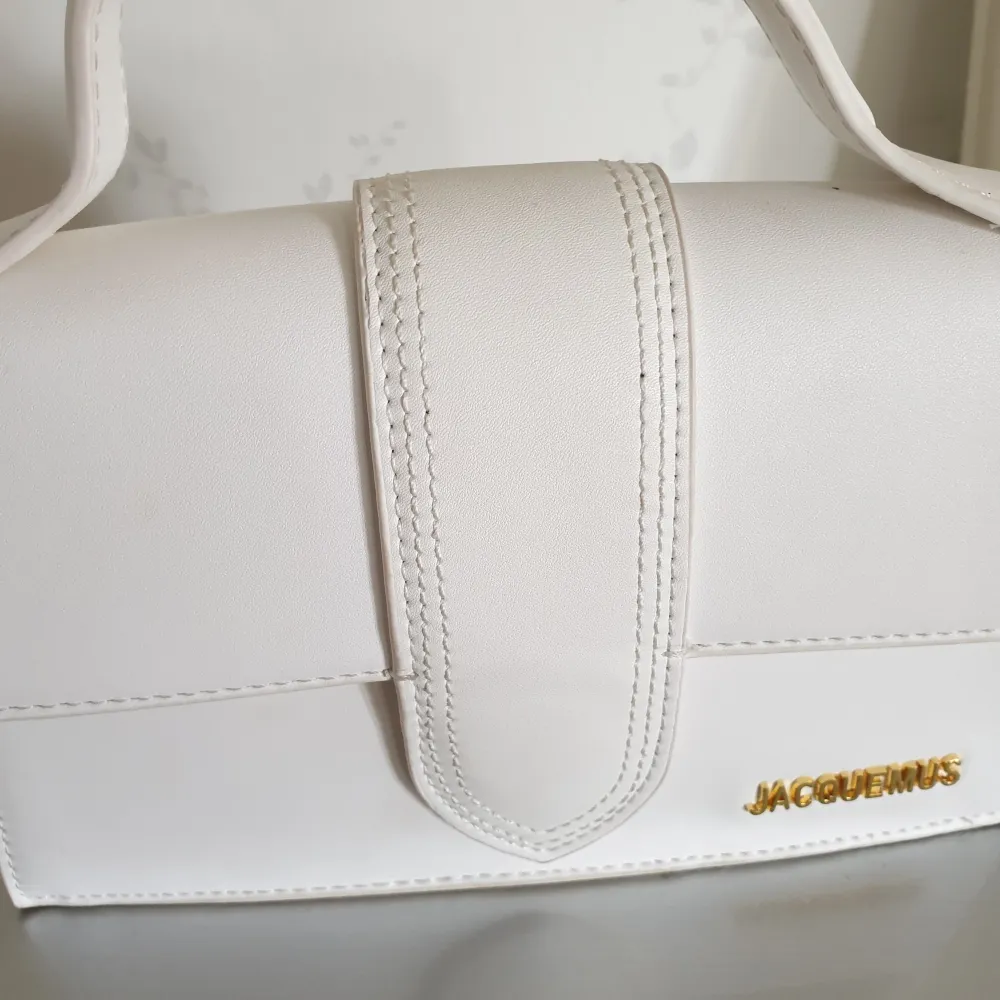 Snygg vit handväska från Jacquemus i stilren design. Väskan har ett handtag och en elegant stängning framtill. Perfekt för att ge en touch av lyx till din outfit. Den har en diskret ficka på baksidan för extra förvaring.. Laukut & Käsilaukut.