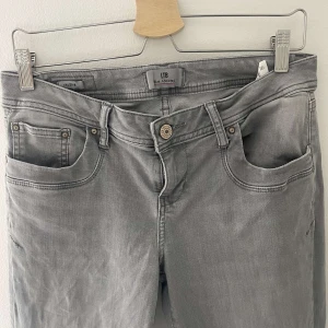 Grå jeans från LTB - Snygga grå jeans från LTB med klassisk femficksdesign och knappgylf. Perfekta för en stilren look. De har en diskret logga på baksidan och är i en neutral grå färg som passar till det mesta. Storlek: W30, L32